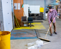 Man sweeping trash at a loading dock in a warehouse.