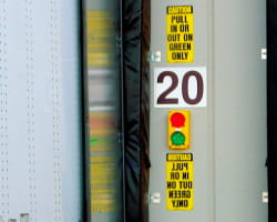 Dock signal lights on the exterior wall of the loading dock area. Yellow signs above and below it say 'Pull in or out on green only'.