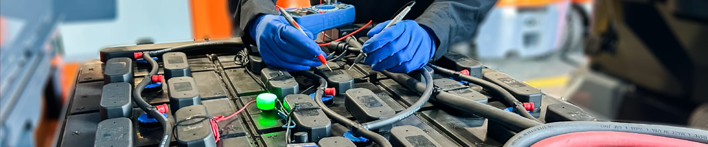 close up of the top of a lead acid battery being worked on by a technician with blue gloves.