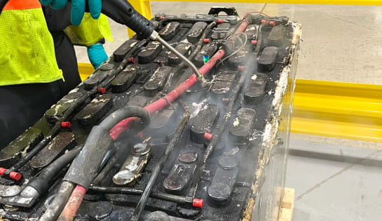 A technician steam cleans a forklift battery