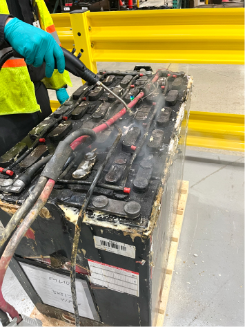 A technician steam cleans a lead acid forklift battery