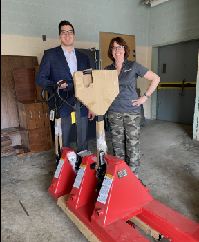 Ben Dymit and Jenni Oliva stand behind three of the pallet jacks that were donated to the Archdiocese of Milwaukee
