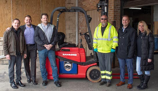 Associated and Hesed House employees stand on either side of a donated Raymond counterbalanced forklift