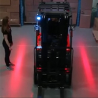 A forklift with two beams of red light shining on the floor on either side of the truck. A pedestrian stands outside the left red zone/light